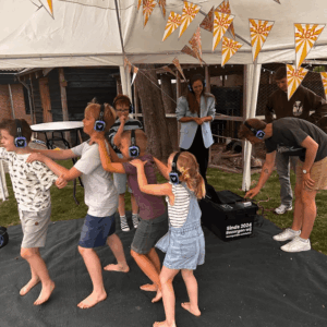 Kinderfeestje met silent disco hoofdtelefoons, dansende kinderen en vrolijke sfeer.